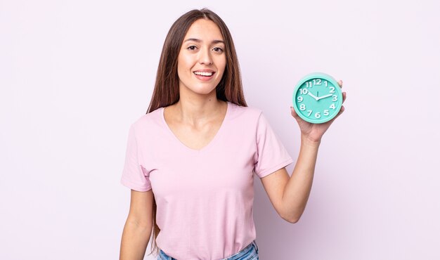 Mujer bonita joven que parece feliz y gratamente sorprendida. concepto de reloj despertador