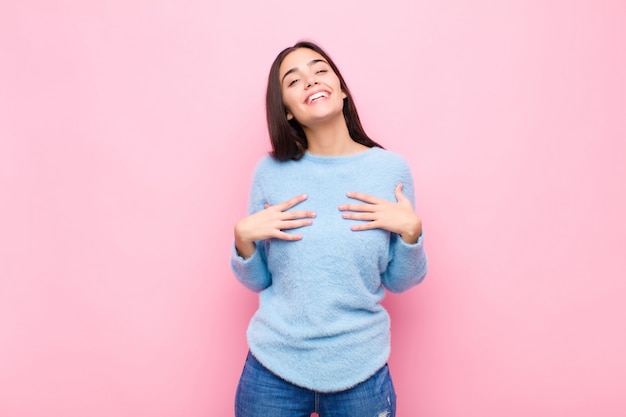 Mujer bonita joven que parece feliz, sorprendida, orgullosa y emocionada, apuntando a sí mismo contra la pared rosa