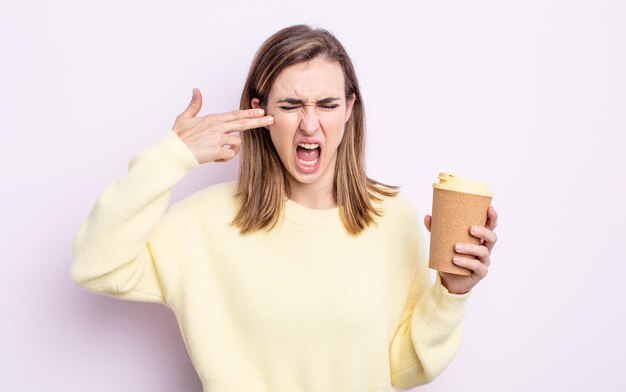 Mujer bonita joven que parece infeliz y estresada, gesto de suicidio haciendo signo de pistola. concepto de café para llevar