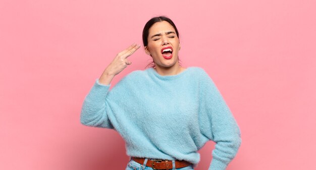 Mujer bonita joven que parece infeliz y estresada, gesto de suicidio haciendo un signo de pistola con la mano, apuntando a la cabeza