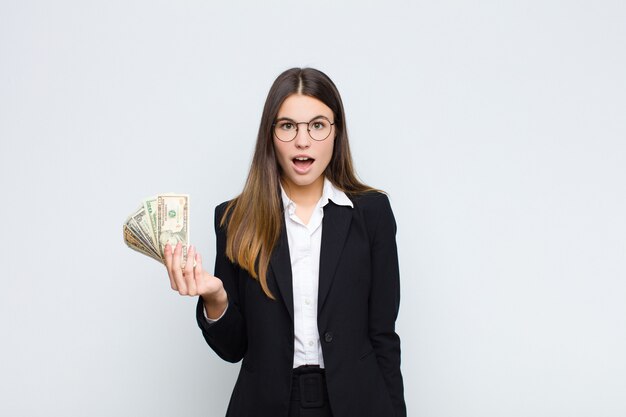 Mujer bonita joven que parece muy sorprendida o sorprendida, mirando con la boca abierta diciendo wow con billetes