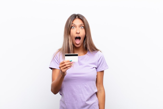 Mujer bonita joven que parece muy sorprendida o sorprendida, mirando con la boca abierta diciendo wow con una tarjeta de crédito