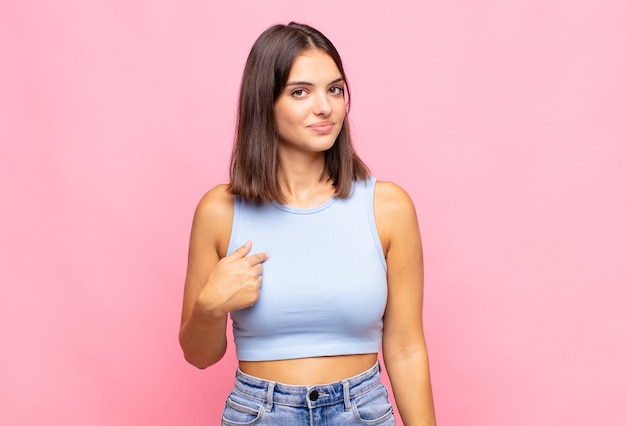 Mujer bonita joven que parece orgullosa, segura y feliz, sonriendo y apuntando a sí misma o haciendo la señal número uno