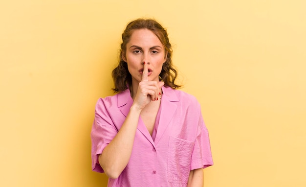 Mujer bonita joven que parece seria y cruzada con el dedo presionado en los labios exigiendo silencio o silencio guardando un secreto