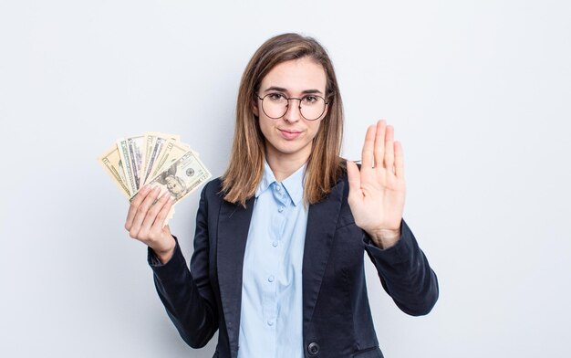 Mujer bonita joven que parece seria mostrando la palma abierta haciendo gesto de parada. concepto de billetes de dólar