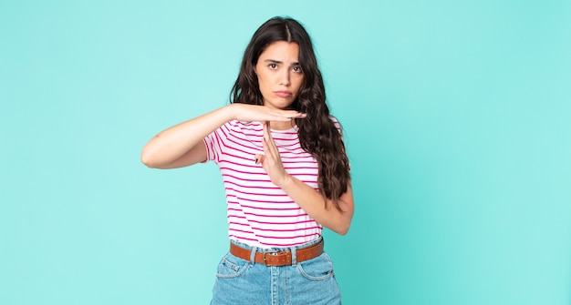 Mujer bonita joven que parece seria, severa, enojada y disgustada, haciendo el signo de tiempo de espera