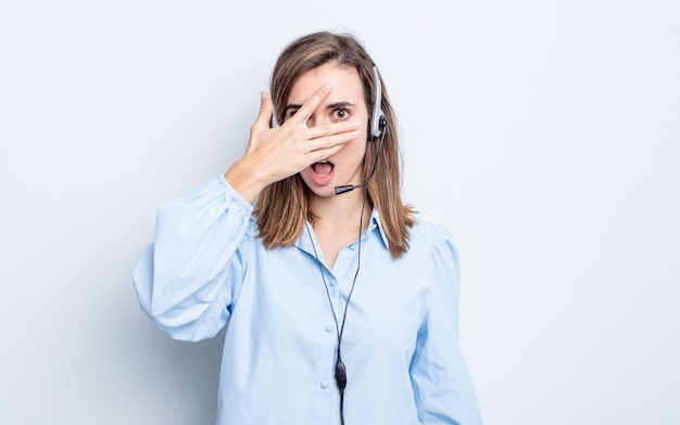 Mujer bonita joven que parece sorprendida, asustada o aterrorizada, cubriendo la cara con la mano. concepto de telemarketer