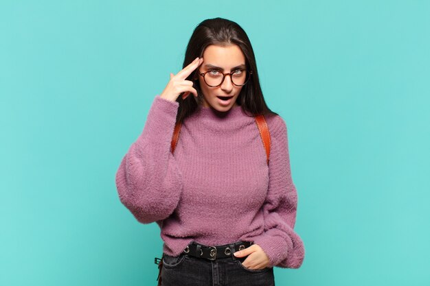 Mujer bonita joven que parece sorprendida, con la boca abierta, conmocionada, dándose cuenta de un nuevo pensamiento, idea o concepto. concepto de estudiante