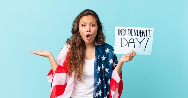 Mujer bonita joven que parece sorprendida y conmocionada, con la mandíbula caída sosteniendo un concepto del día de la independencia de objeto