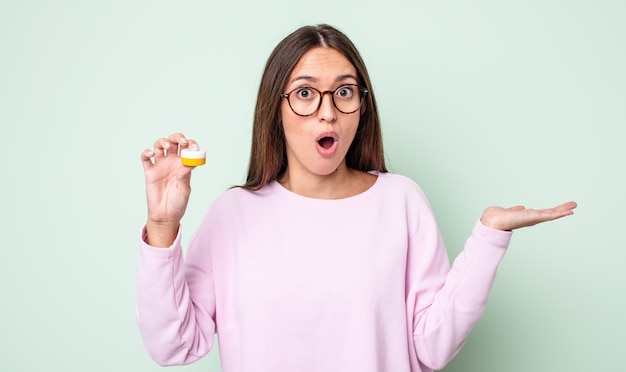 Mujer bonita joven que parece sorprendida y conmocionada, con la mandíbula caída sosteniendo un objeto. concepto de lentes de contacto