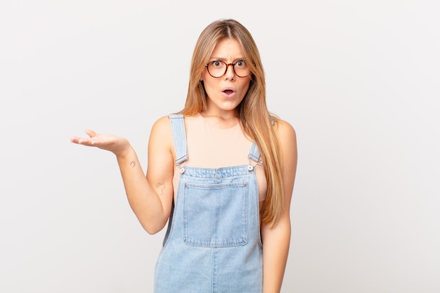 Mujer bonita joven que parece sorprendida y consternada, con la mandíbula caída sosteniendo un objeto