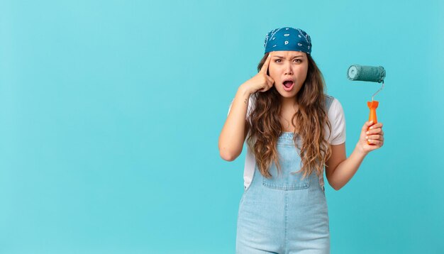 Mujer bonita joven que parece sorprendida, dándose cuenta de un nuevo pensamiento, idea o concepto y pintando una pared