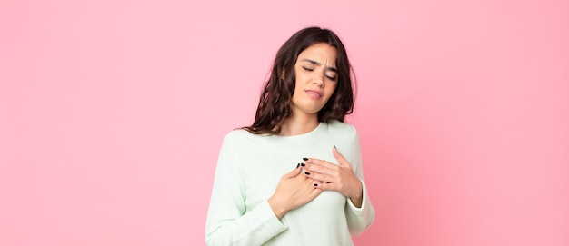 Foto mujer bonita joven que parece triste, herida y con el corazón roto, sosteniendo ambas manos cerca del corazón, llorando y sintiéndose deprimida