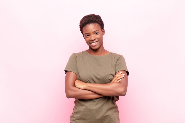 Mujer bonita joven que parece un triunfador feliz, orgulloso y satisfecho sonriendo con los brazos cruzados sobre la pared rosa