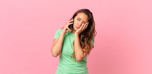 Mujer bonita joven que se siente aburrida, frustrada y con sueño después de un cansado y sosteniendo un teléfono inteligente