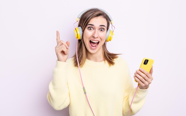 Mujer bonita joven que se siente como un genio feliz y emocionado después de realizar una idea. concepto de auriculares y teléfono