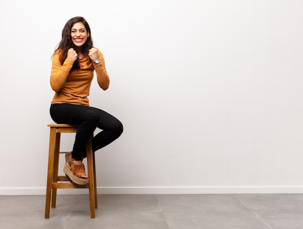 Mujer bonita joven que se siente como un genio sosteniendo el dedo con orgullo en el aire después de darse cuenta de una gran idea, diciendo eureka sentada en una habitación