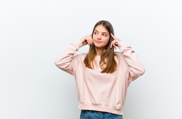 Mujer bonita joven que se siente confundida o dudando, concentrándose en una idea, pensando mucho, mirando al espacio en blanco del lado contra la pared blanca