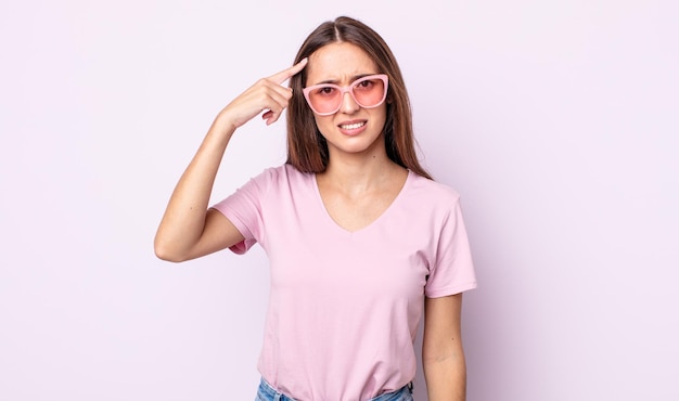 Mujer bonita joven que se siente confundida y perpleja, mostrando que estás loco. concepto de gafas de sol rosa