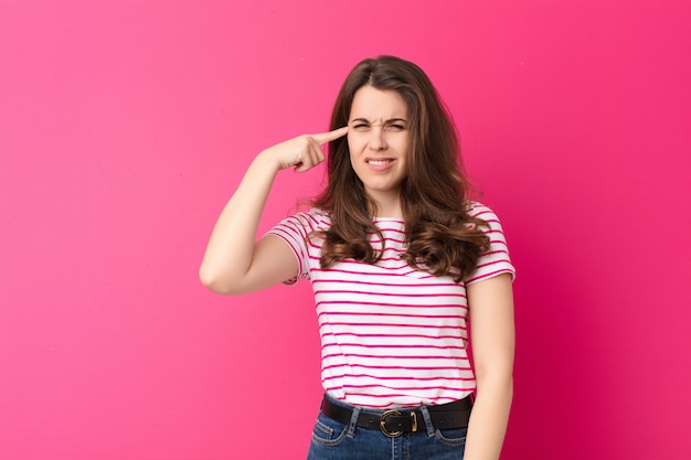 Mujer bonita joven que se siente confundida y perpleja, mostrando que estás loco, loco o loco contra la pared rosa