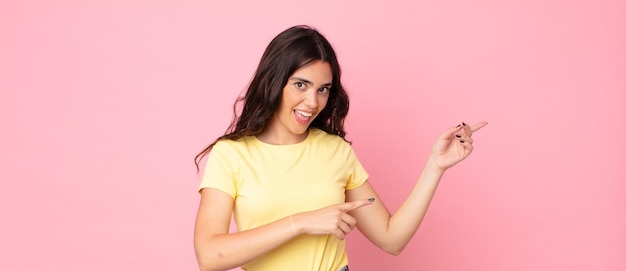 Mujer bonita joven que se siente conmocionada y sorprendida, apuntando al espacio de la copia en el lateral con una mirada asombrada y con la boca abierta