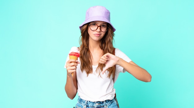 Mujer bonita joven que se siente cruzada, mostrando los pulgares hacia abajo sosteniendo un helado. concepto de verano