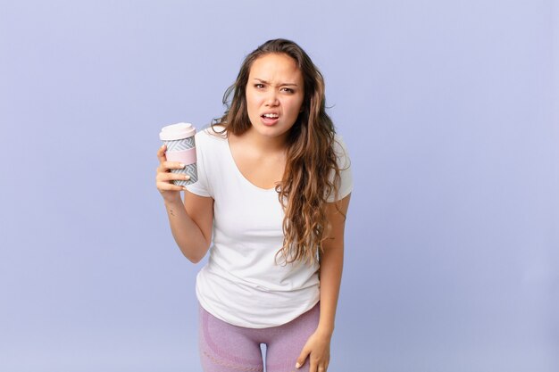 Mujer bonita joven que se siente desconcertado y confundido y sosteniendo un café