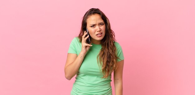 Mujer bonita joven que se siente desconcertado y confundido y sosteniendo un teléfono inteligente