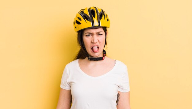 Mujer bonita joven que se siente disgustada e irritada y saca la lengua concepto de casco de bicicleta