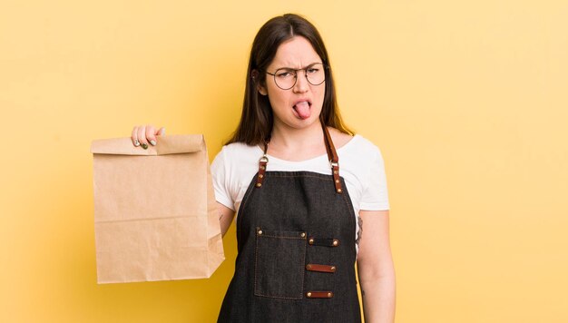 Mujer bonita joven que se siente disgustada e irritada y saca la lengua mensajero de comida rápida