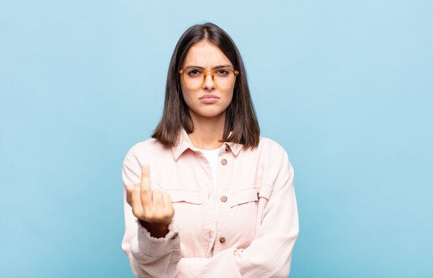 Mujer bonita joven que se siente enojada, molesta, rebelde y agresiva, moviendo el dedo medio, contraatacando