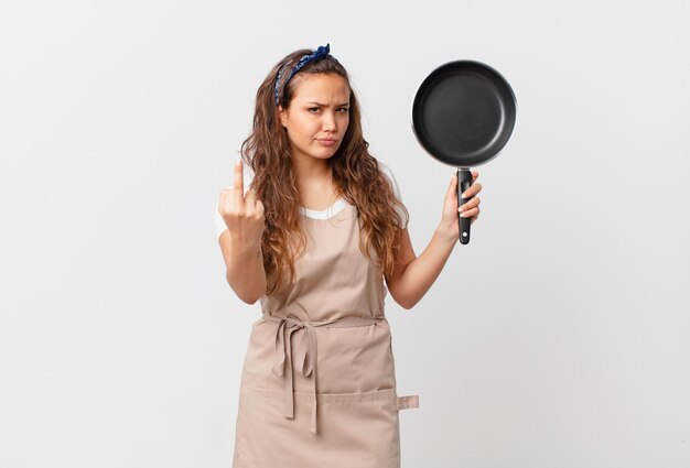 Foto mujer bonita joven que se siente enojado, molesto, rebelde y agresivo concepto de chef y sosteniendo una sartén