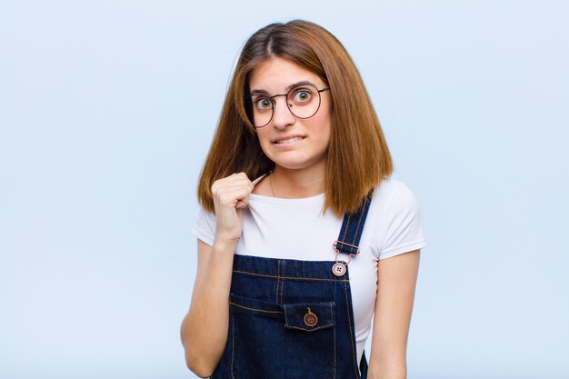 Mujer bonita joven que se siente estresada, ansiosa, cansada y frustrada, tirando del cuello de la camisa, mirando frustrado con un problema contra el azul