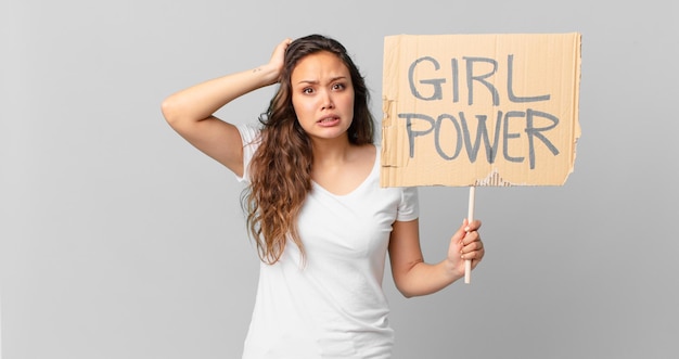 Mujer bonita joven que se siente estresada, ansiosa o asustada, con las manos en la cabeza y sosteniendo una pancarta de poder femenino