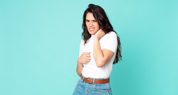 Mujer bonita joven que se siente estresada, frustrada y cansada, frotando el cuello doloroso, con una mirada preocupada y preocupada