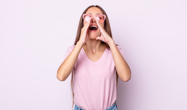 mujer bonita joven que se siente feliz, dando un gran grito con las manos al lado de la boca. concepto de gafas de sol rosa