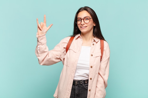 Mujer bonita joven que se siente feliz, divertida, segura, positiva y rebelde, haciendo un letrero de rock o heavy metal con la mano. concepto de estudiante