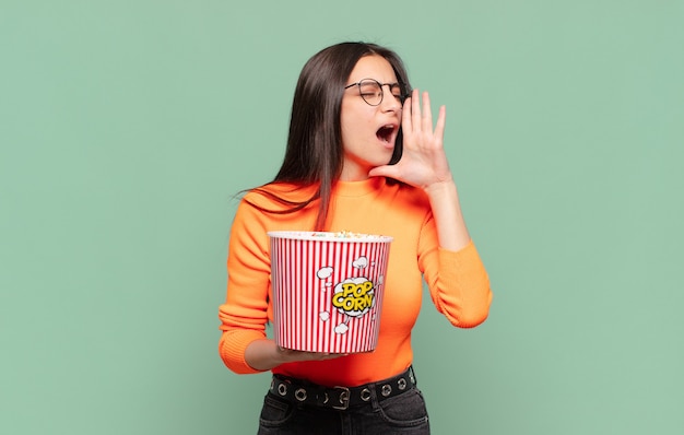 Mujer bonita joven que se siente feliz, emocionada y positiva, dando un gran grito con las manos al lado de la boca, gritando. concepto de palomitas de maíz