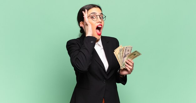 Mujer bonita joven que se siente feliz, emocionada y sorprendida, mirando hacia el lado con ambas manos en la cara. concepto de negocio y billetes