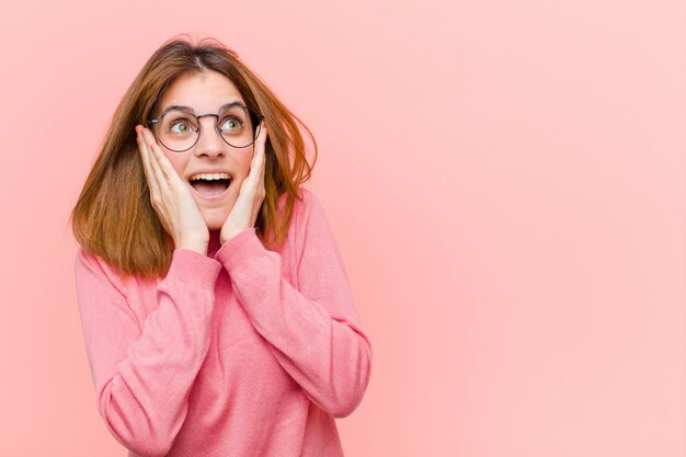 Mujer bonita joven que se siente feliz, emocionada y sorprendida, mirando a un lado con ambas manos en la cara