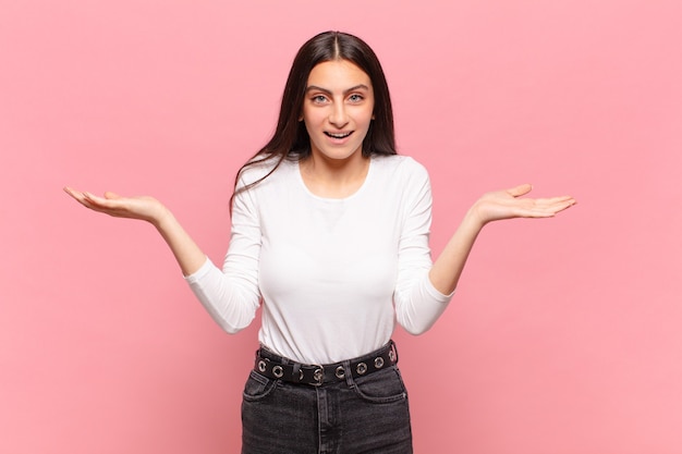 Mujer bonita joven que se siente feliz, emocionada, sorprendida o conmocionada, sonriendo y asombrada por algo increíble