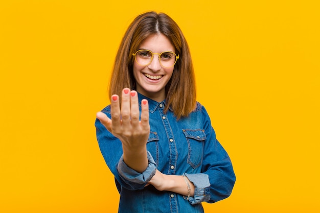 Mujer bonita joven que se siente feliz, exitosa y segura, enfrenta un desafío y dice ¡adelante! o darte la bienvenida contra la pared amarilla