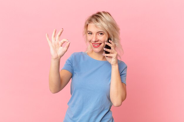 Mujer bonita joven que se siente feliz, mostrando aprobación con gesto bien. concepto celular