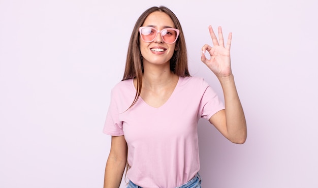 Mujer bonita joven que se siente feliz, mostrando aprobación con gesto bien. concepto de gafas de sol rosa