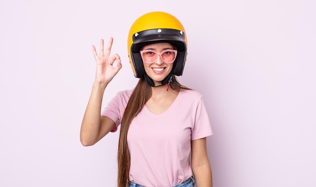 Mujer bonita joven que se siente feliz, mostrando aprobación con gesto bien. motociclista y casco