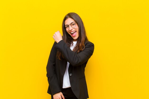 Mujer bonita joven que se siente feliz, positiva y exitosa, motivada cuando enfrenta un desafío o celebra buenos resultados contra la pared naranja