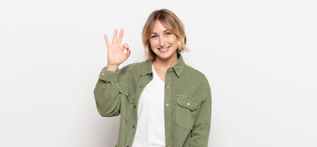 Mujer bonita joven que se siente feliz, relajada y satisfecha, mostrando aprobación con gesto bien, sonriendo