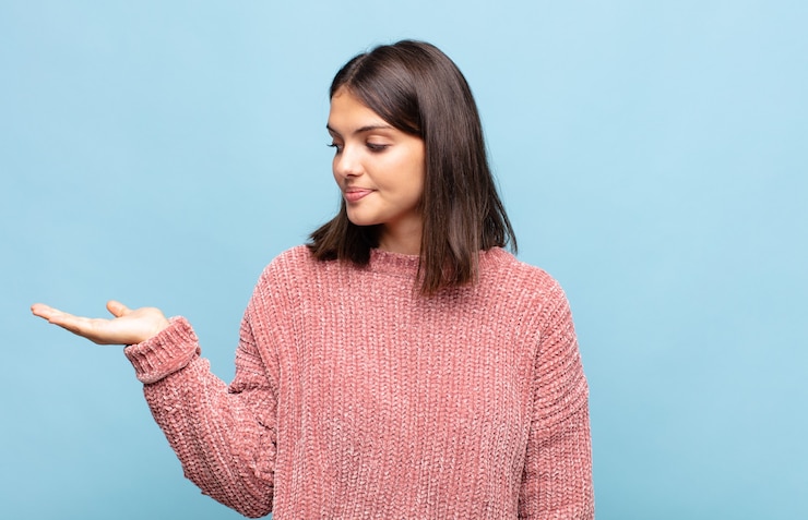 Foto mujer bonita joven que se siente feliz y sonriendo casualmente, mirando a un objeto o concepto sostenido en la mano al costado