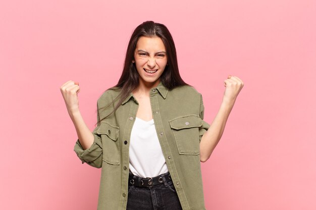 Mujer bonita joven que se siente feliz, sorprendida y orgullosa, gritando y celebrando el éxito con una gran sonrisa