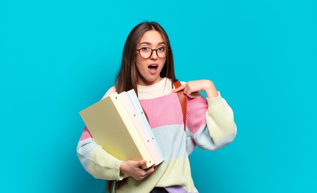 Mujer bonita joven que se siente feliz, sorprendida y orgullosa, señalando a sí misma con una mirada emocionada y asombrada